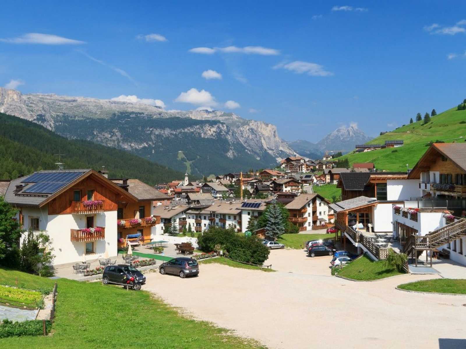 נוף הכפר סן קסיאנו (San Cassiano) על רקע הרי הדולומיטים ביום קיץ בהיר.