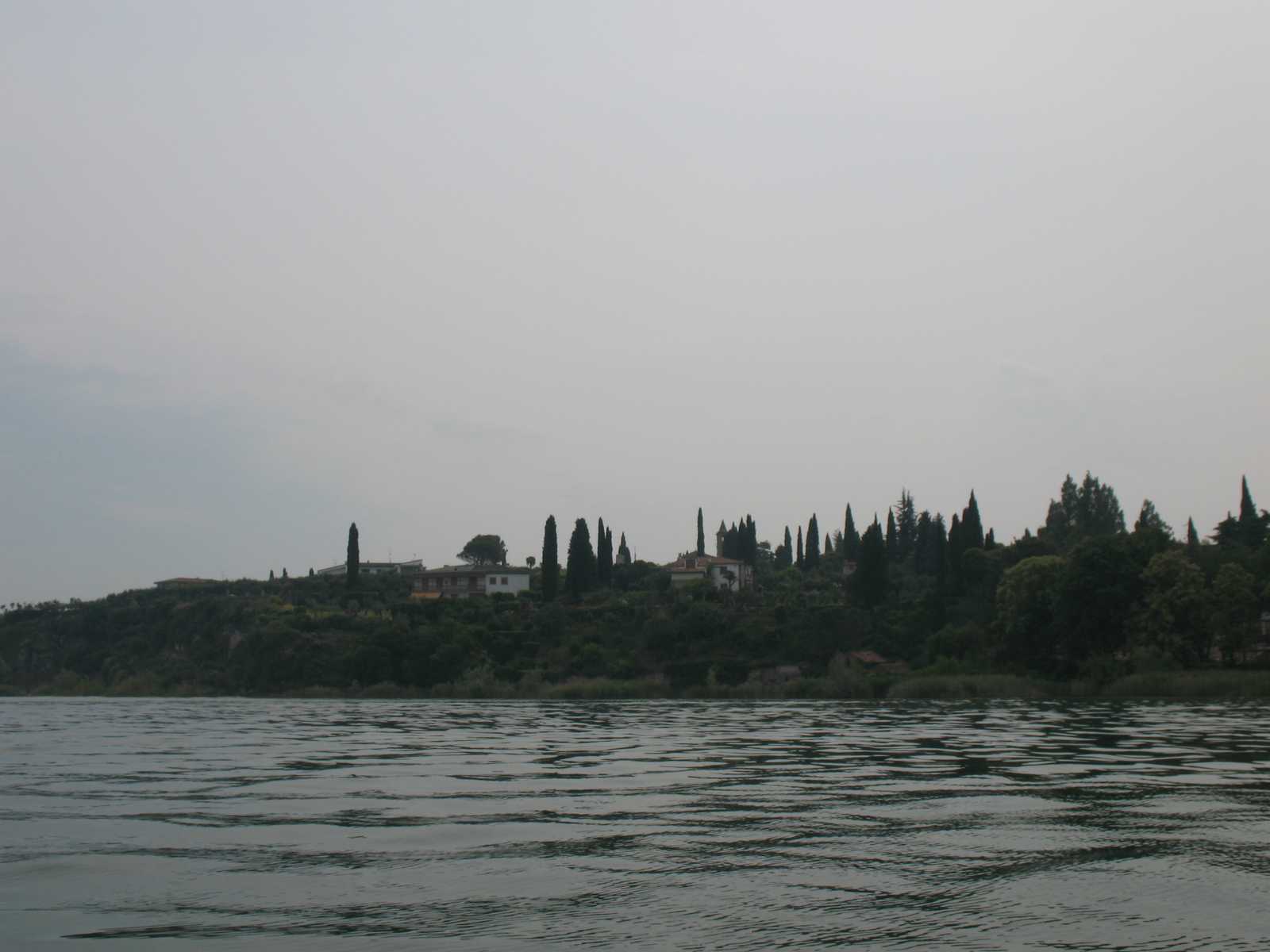 קו חוף ירוק עם עצים ומים רגועים באזור אגם גארדה