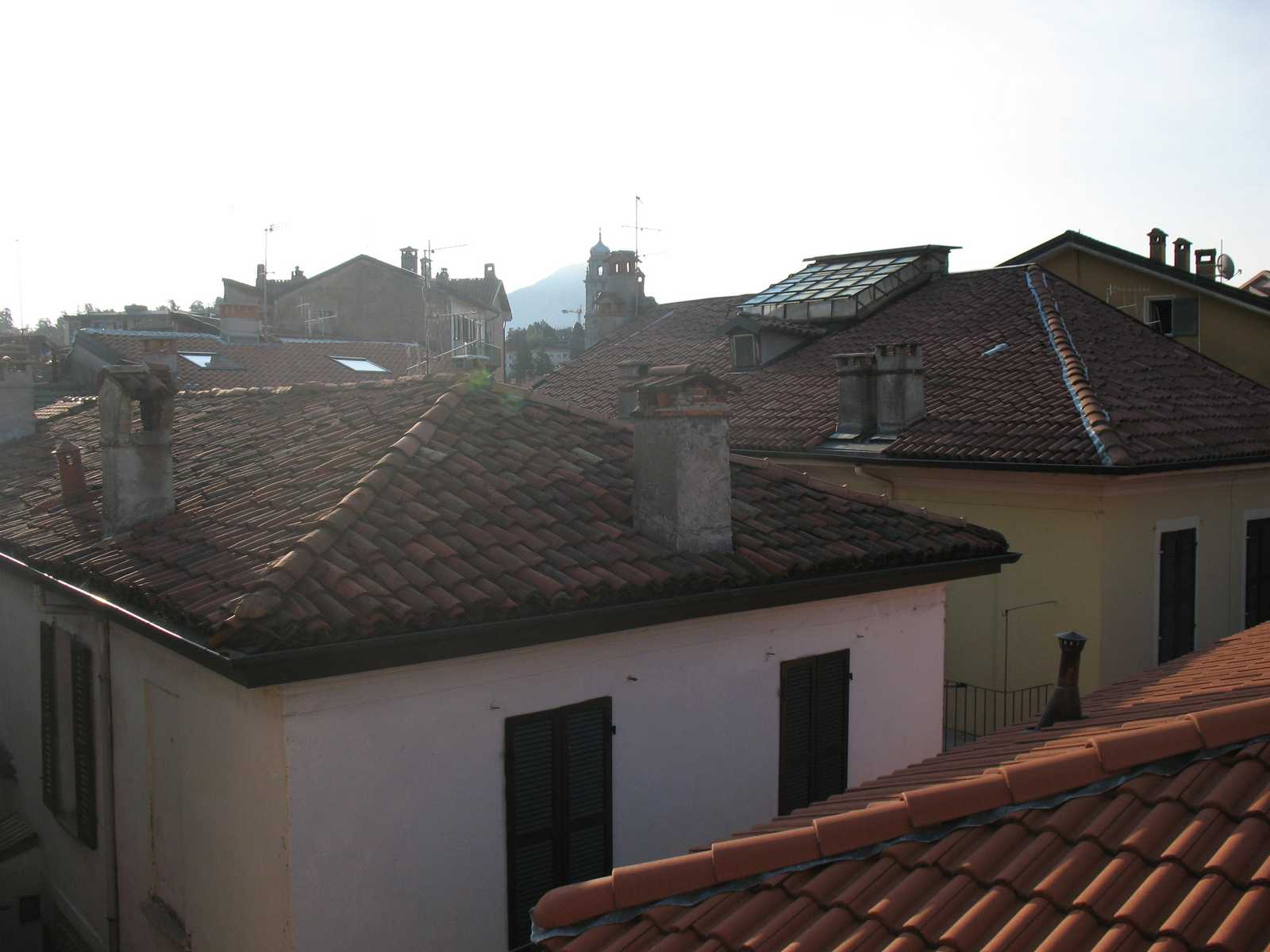 גגות אדומים של עיירה איטלקית מסורתית ליד אגם קומו, עם מגדל כנסייה והרים ברקע באור רך