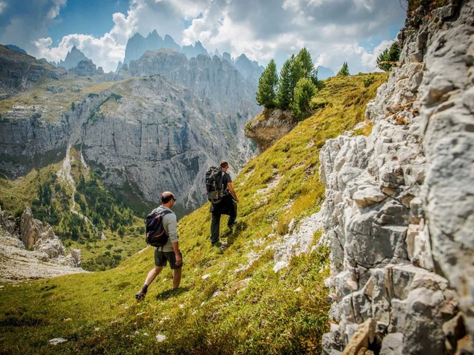 מטיילים בשביל הררי עם נוף דרמטי של צוקים ועמק ירוק בדולומיטים