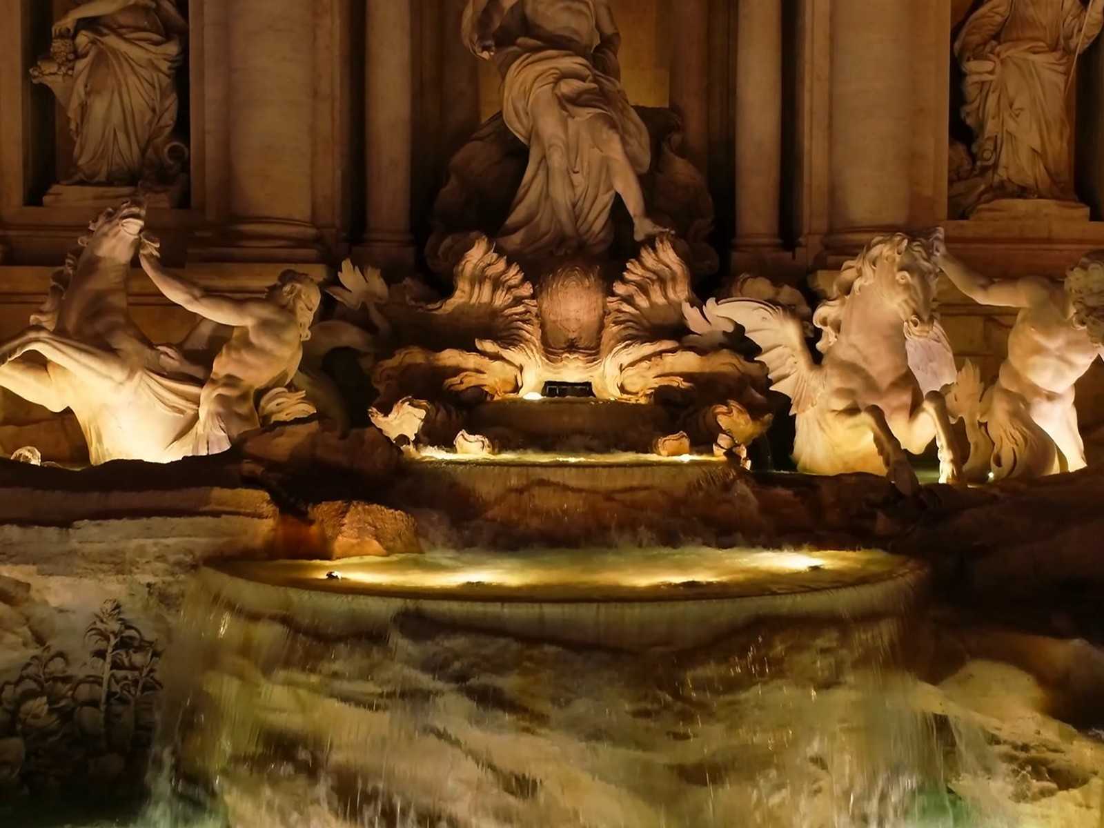 הפסלים המפורסמים של מזרקת טרווי ברומא מוארים באור חמים בשעות הערב.