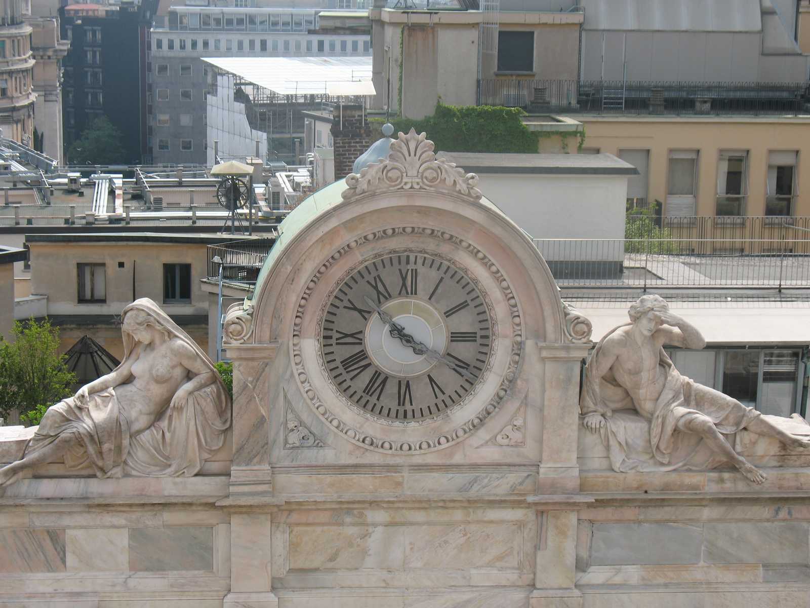 השעון המעוטר על חזית מבנה היסטורי בכיכר הדואומו במילאנו.