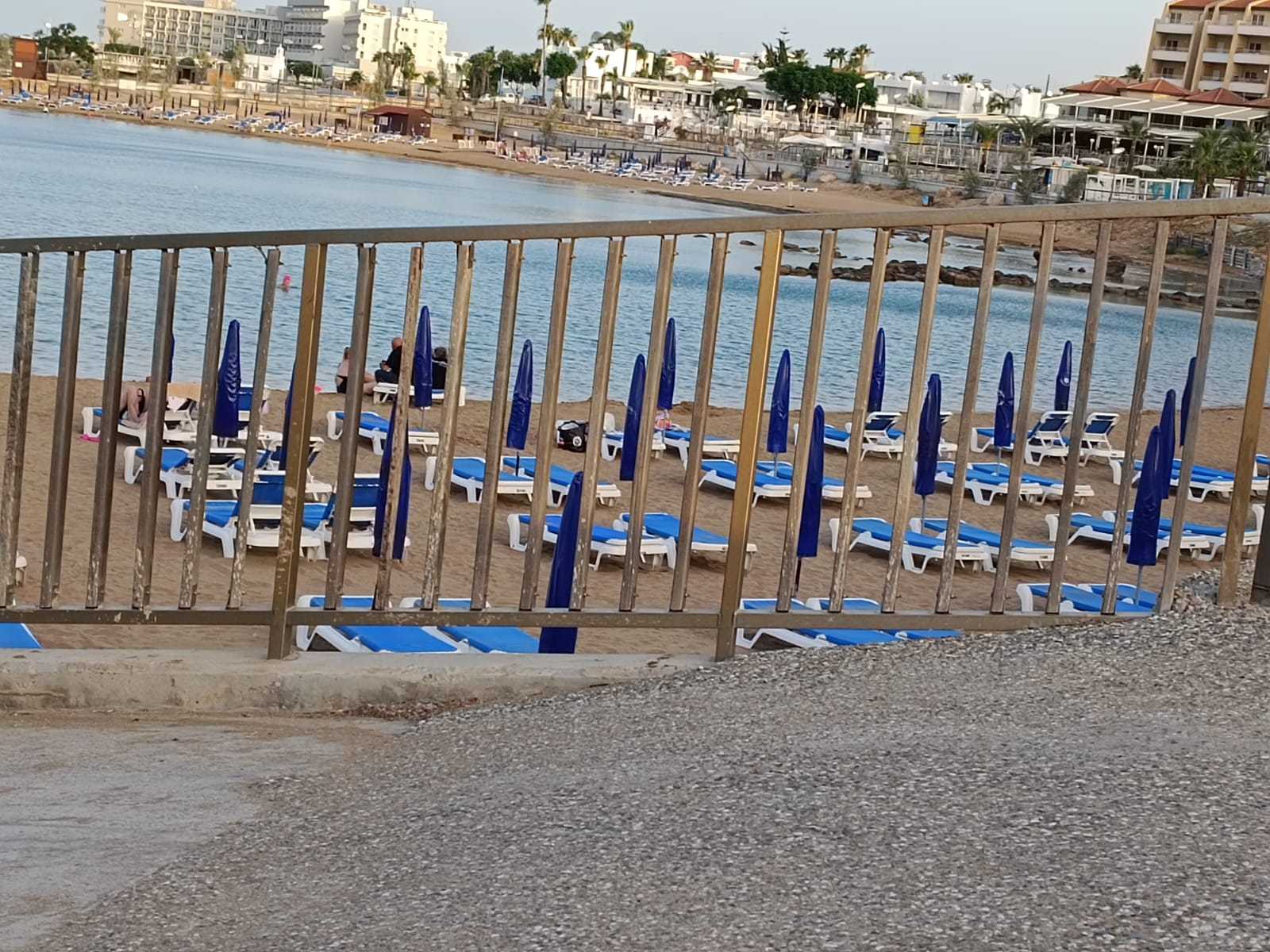 שורות של שמשיות כחולות סגורות על חוף הים בקלבריה מאחורי גדר עץ.