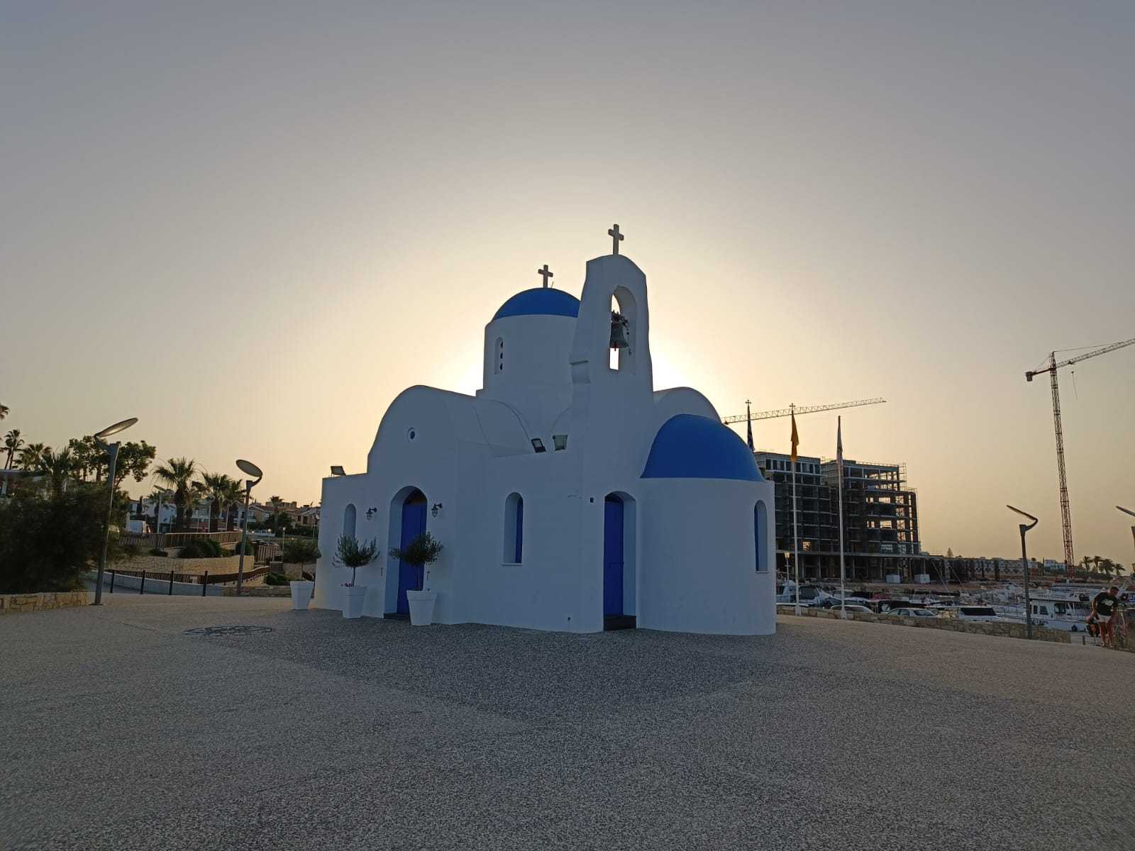 כנסייה לבנה עם כיפות כחולות בקלבריה בשעת שקיעה, מול אור השמש.